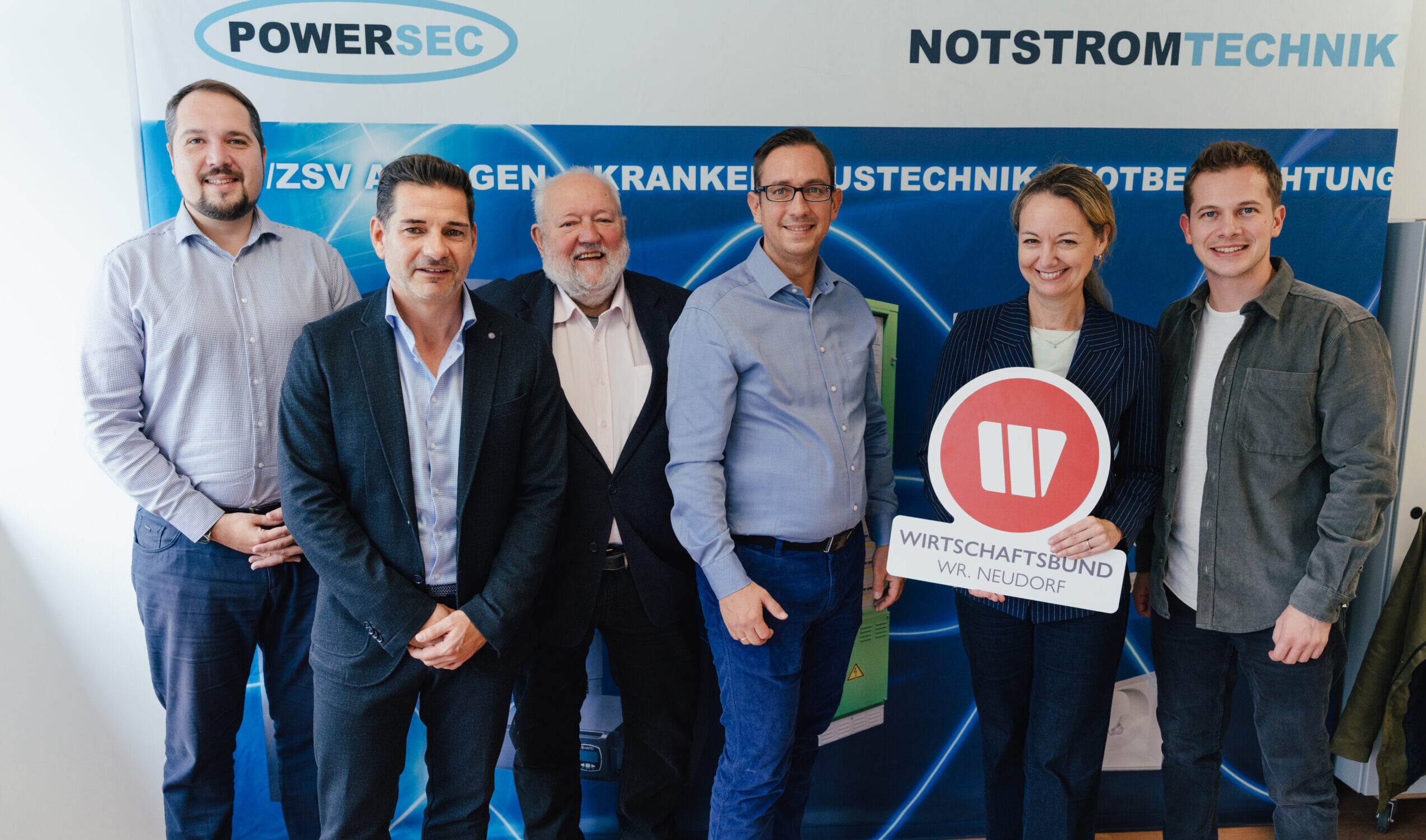 Am Bild zu sehen vor einer Werbetafel der Firma Powersec v.l. GF Stefan Pfefferer, GF Thomas Wimmer, Erhard Gredler, Markus Sellmeister, WB Obfrau Nina Strass-Wasserlof und Tobias Printz