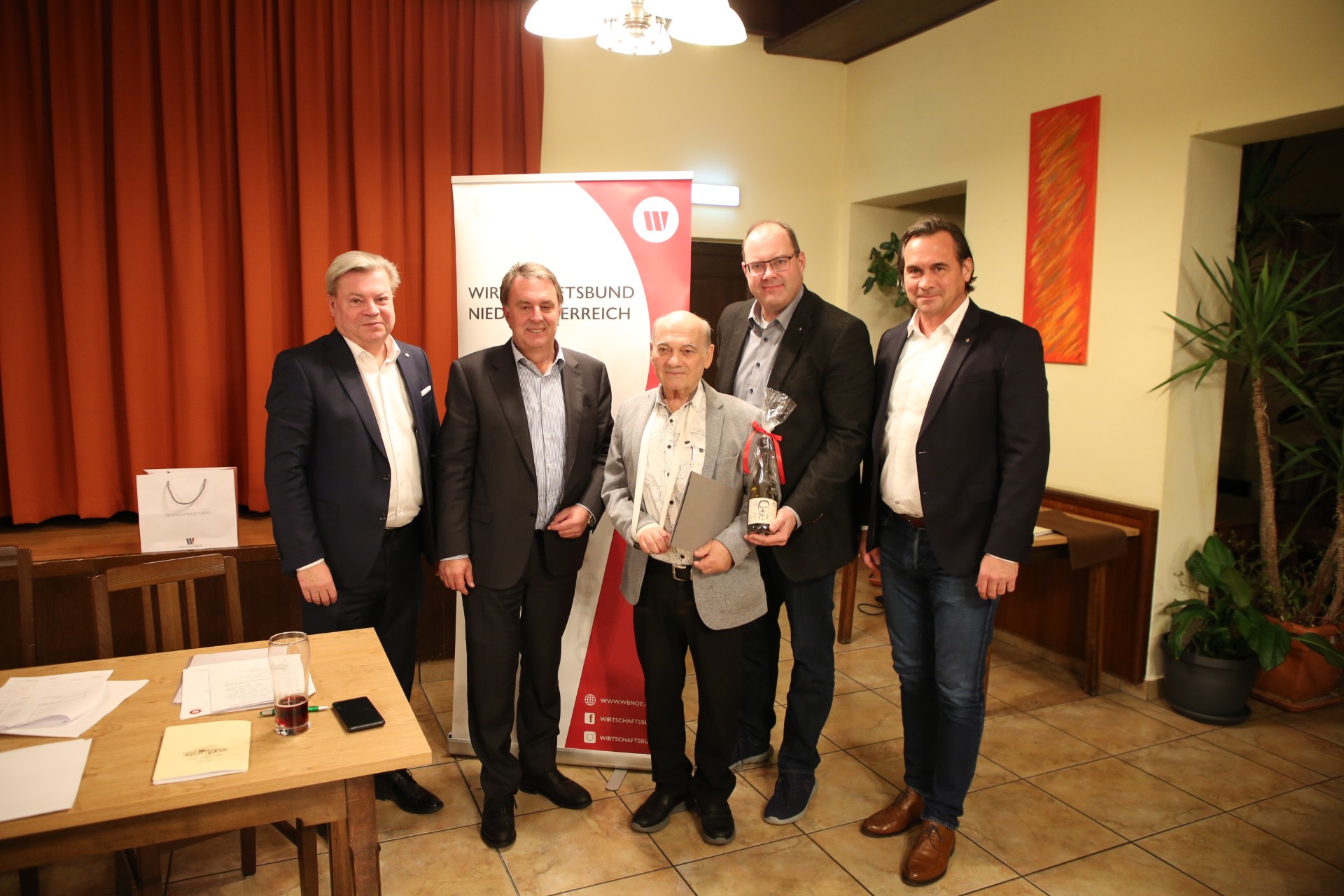 Vor dem Wirtschaftsbundbanner stehend eine Delegation des Wirtschaftsbundes und dem geehrten in der Mitte. Das Bild wurde innen in einem Saal aufgenommen